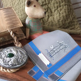 Classic silver grey cotton handkerchief with blue stripe running along the border, has a hand stitch pattern of night scenery at the corner