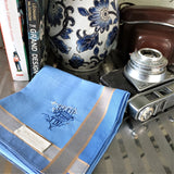 Sky blue cotton handkerchief with two silver grey stripes as border, hand embroidered an exquisite line drawing of a jet flying over an old Chinese village and trees