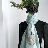 A light turquoise blue pure linen scarf hand embroidered an abstract line art pattern with different color and metal threads, is dressed on a mannequin.