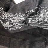 Close up of air weight black silk wool scarf has embroidered a big white line art scenery pattern of an ancient Chinese village next to the hills with power towers on the peak.