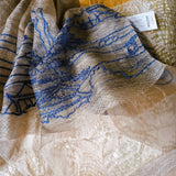 Close up of light weight and sheer olive color silk wool scarf, embroidered a big blue line art landscape pattern of an ancient Chinese village, includes lodges, animal and power towers on the hills