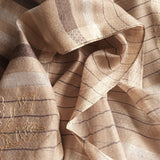 Close-up of a milk tea color silk wool scarf featured by tiny shimmering texture, brown pin-stripes, and well-made edges, has a hand embroidery of multi-color flower pattern. 