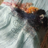 Close up of icy blue color pure linen scarf with a  hand-felted landscape pattern highlighted by mini hand-stitched water swirl  