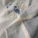 Close-up of a grey tone yarn dyed 300s pure cashmere scarf with beige velveteen beige weave in stripes, hand embroidered two blue birds and white flowers 