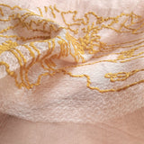 Close up of light weight textured light salmon color silk wool scarf has embroidered a big golden yellow thread art of landscape pattern in bold stitches