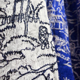 Close up on line drawing embroidery of spaceman walking on a grassland on the white ground of a pure linen scarf