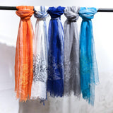 A selection of linen scarves in various colors, each featuring a line art embroidery design of a spaceman getting lost in an old village. 