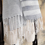 Close up on the hand twisted tassel of a light weight white and navy color stripe cotton linen scarf 