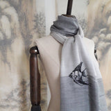 A light grey tone super fine cashmere scarf has a hand embroidery of angelfish pattern well wrapped on the neck of a classic mannequin.