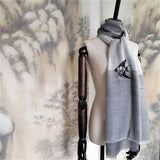 A soft and lightweight pure cashmere shawl in varies grey tone, has embroidered a lively black and white swimming angelfish pattern in the center of the scarf.