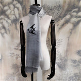 A classic unisex grey tone super fine cashmere scarf has a black and white thread work of a swimming angelfish pattern at the front 