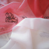 Close up on the texture and softness of a red and white super delicate pure cashmere scarf that embroidered with four swimming goldfishes line art pattern.